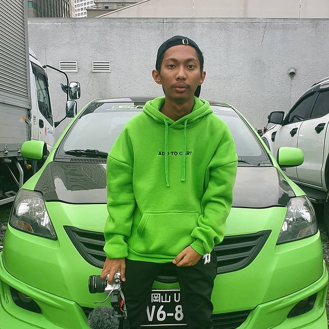 Emman Nimedez in a green hoodie and black jeans sitting on his brand new green car.